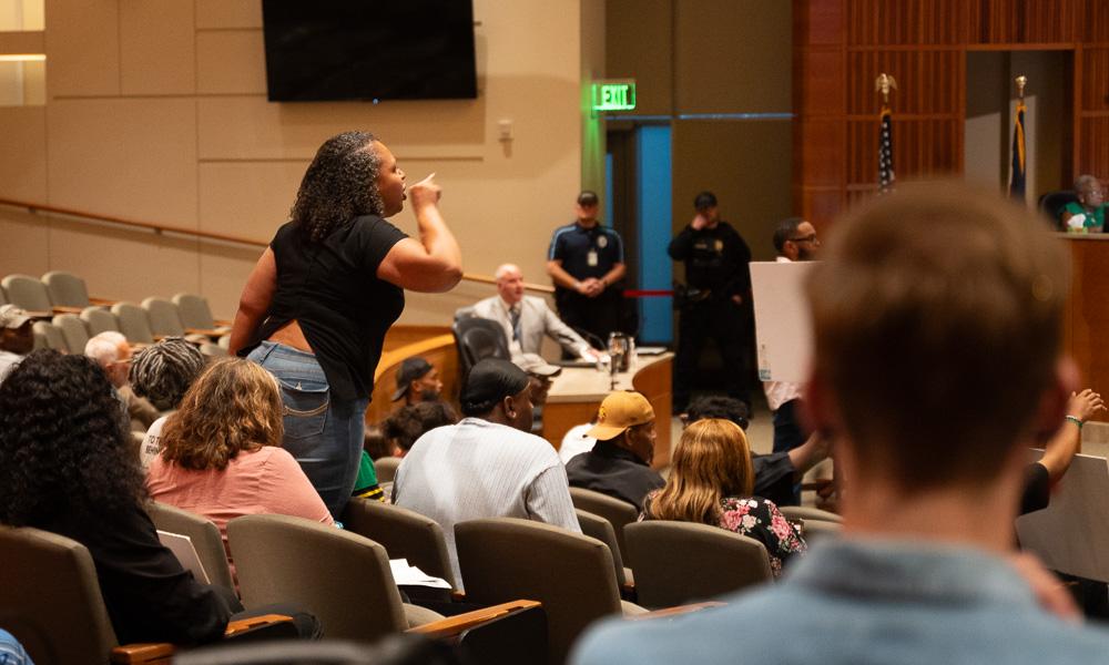 A woman stands from the audience to address Aurora City Council, police officers visible nearby