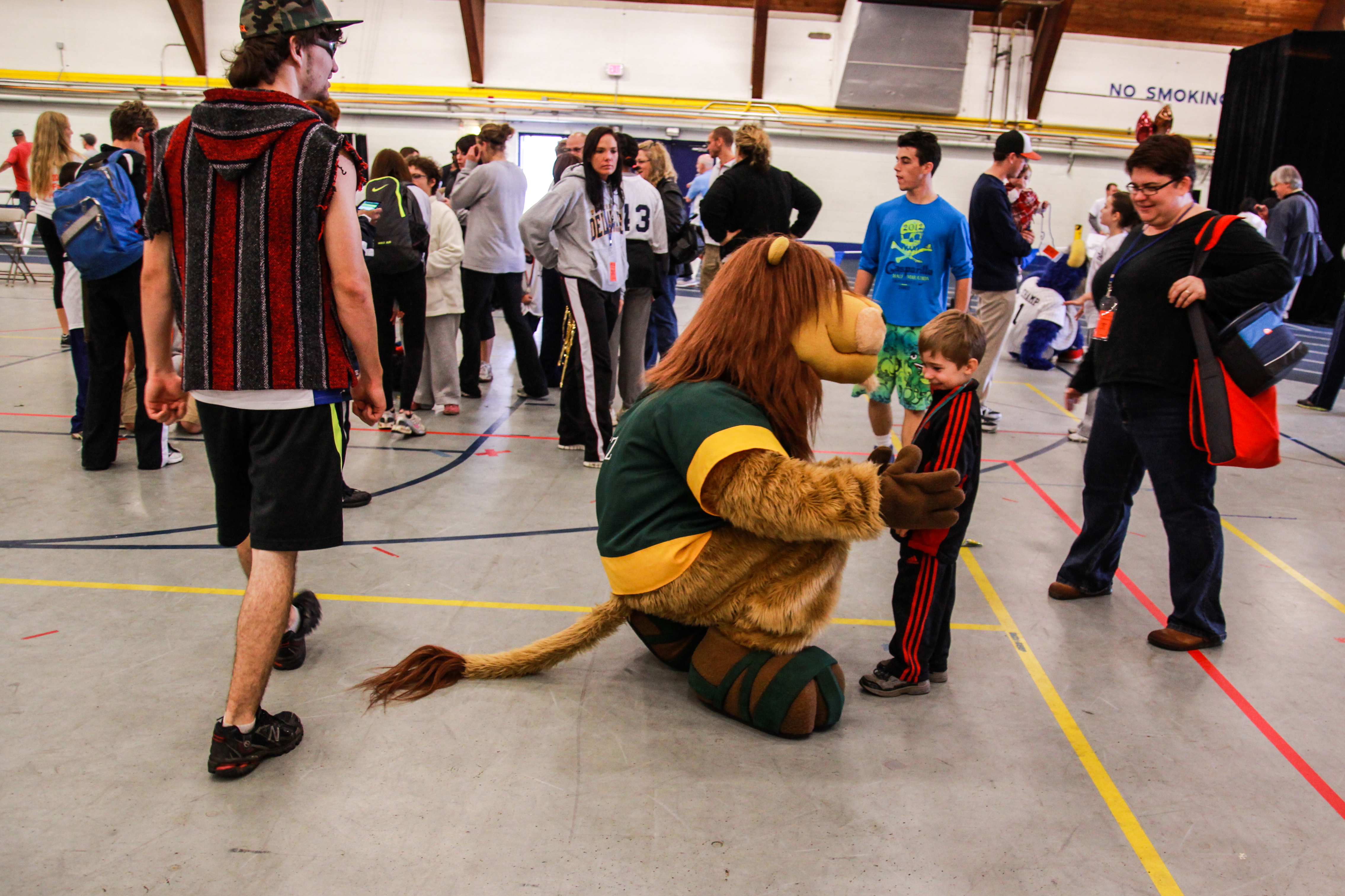 A mascot in a lion costume kneels to hug a young boy at the Special Olympics
